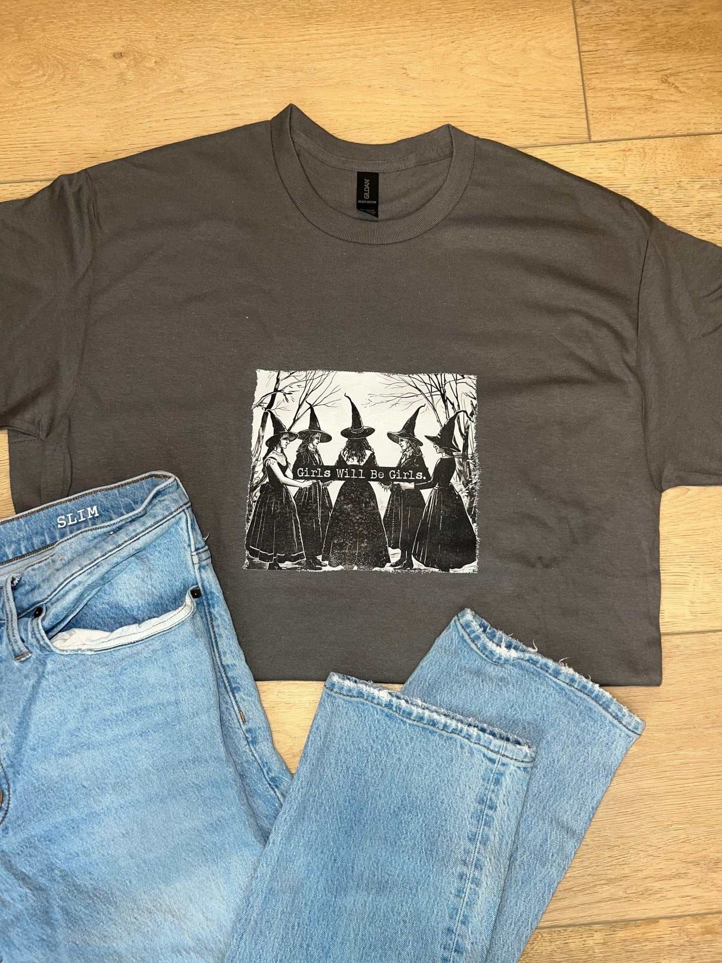 Girls Will Be Girls custom graphic Halloween t-shirt in dark charcoal with witch design.